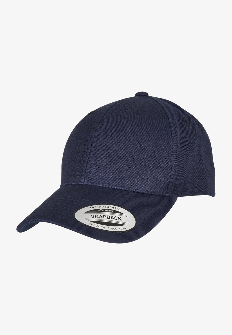 Темno modra snapback kapica iz teksturirane tkanine, z ukrivljenim vizirjem in izrazitim srebrnim logotipom na sprednji strani.