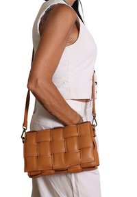 Borsa a tracolla in pelle intrecciata di colore tan, con forma rettangolare e tracolla regolabile, caratterizzata da una texture liscia e dettagli di cucitura sottili.