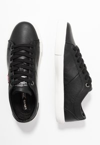 Sneaker in pelle nera con suole in gomma bianca, caratterizzati da punta tonda, chiusura con lacci e dettagli texturizzati sulla parte superiore.