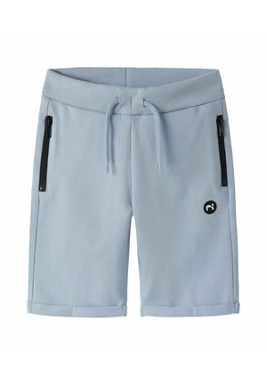 Shorts décontractés bleu clair avec taille côtelée, cordon de serrage, poches latérales zippées noires, ourlets retroussés et petit logo noir sur la jambe gauche.