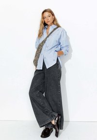 Chemise boutonnée rayée bleu clair avec broderie florale, associée à un pantalon en denim gris taille haute et large, et des mocassins noirs.
