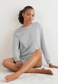 Ljusgrå långärmad sweatshirt med rund hals och lös passform, tillsammans med korta shorts, vilande på en mjuk vit matta.