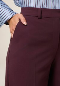 Bordeaux op maat gemaakte broek met zijzakken, voorzien van een gladde textuur en een gestructureerde tailleband, gecombineerd met een blauw gestreefd shirt.