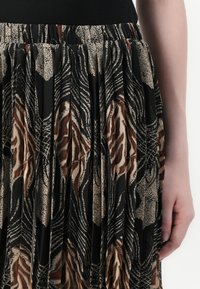 Falda negra con pliegues que presenta un estampado abstracto de animales en beige y óxido, con una cinturilla texturizada. La tela parece ligera y fluida.