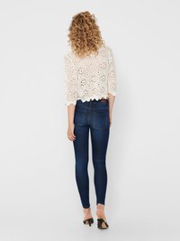 Lättviktskrämfärgad virkade topp med vågig nederkant och ärmar som går till tre fjärdedelar, ihop med mörkblå skinny jeans och svarta klacksandaler.