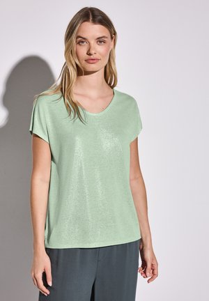 Lichtgroene top met korte mouwen in een zachte, glanzende stof met een V-halsontwerp, gecombineerd met een donker, loszittende broek. Eenvoudige en casual stijl.