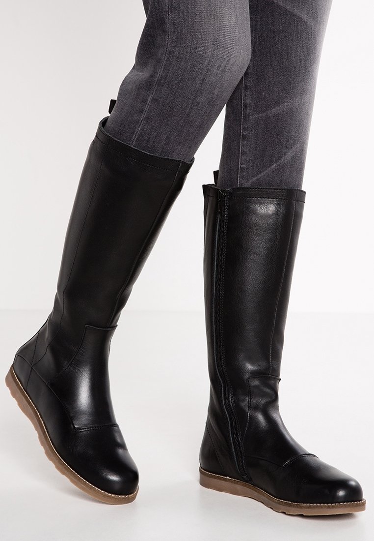 Botas de cuero negro hasta la rodilla con un acabado suave, cremallera lateral y suela de goma marrón. Presentan una punta redondeada y detalles de costura mínimos.