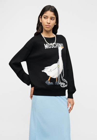 Μαύρο πλεκτό φούτερ με στυλιζαρισμένο λευκό γραφικό χήνας, τη λέξη "MOSCHINO" και σχέδιο με πέρλες σε μορφή κολιέ. Συνδυάζεται με ανοιχτό μπλε φούστα.