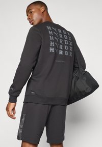 Black sweatshirt with text "HYROX" printed in various sizes on the back. Paired with matching shorts. Includes a black bag. Cotton blend material.