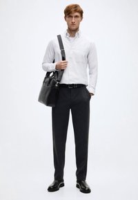 Λευκό πουκάμισο με κουμπιά, μαύρη ζώνη, σκούρο γκρι παντελόνι και μαύρα δερμάτινα παπούτσια. Κρατώντας μια μαύρη δερμάτινη τσάντα με ιμάντα ώμου.