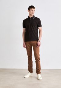 Black polo shirt with white accents, paired with brown slim-fit pants and white sneakers. Simple design with a modern fit.