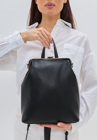 Rucsac negru din piele cu un finisaj texturat, mânere superioare duale, accesorii metalice și un design minimalist.