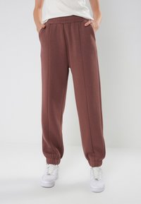 Braune Sweatpants mit entspannter Passform, elastischem Bund, zwei Seitentaschen und schmal zulaufenden Bündchen; aus weichem, strukturiertem Stoff gefertigt.