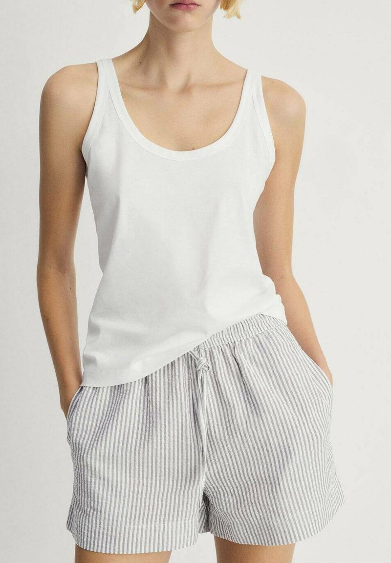Hvid ærmeløs tanktop parret med lysegrå og hvide stribede shorts, der har en snoretræk i taljen og sidelommer.