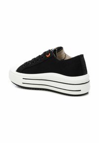 Zapatilla de lona negra con suela de plataforma blanca, con ojetes negros y naranjas, suela de goma texturizada y un sutil detalle de la marca.