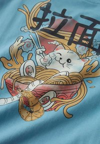Tissu bleu clair avec un chat de dessin animé joyeusement en train de manger des nouilles dans un bol décoré, avec des baguettes et des accents de crevettes.