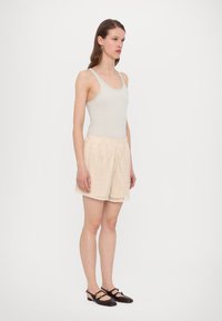 Lichtgrijze getailleerde tanktop gecombineerd met beige textuurn shorts met een patroon en een scalloped zoom; gedragen met donkere bruine flats.