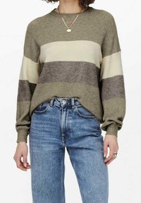 Olive green striped sweater with cream and taupe horizontal bands, ribbed texture, dropped shoulders, and long sleeves, paired with blue jeans.