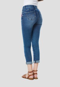 Úzke džínsy v tmavomodrej farbe s ošúchaným lemom, s vreckami na zadnej strane a vyšívaným detailom. Kombinované s hnedými sandálmi na remienky.