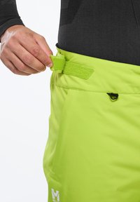 Helle grüne Outdoor-Hose mit einem Klettverschluss an der Taille und einem schwarzen Clip. Glatte Textur, strapazierfähiger Stoff, Logo an der Seite.
