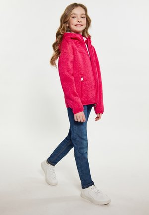 Felle roze fleece zip-up jack met capuchon en twee zijzakken, gecombineerd met blauwe slim-fit jeans en witte sneakers.