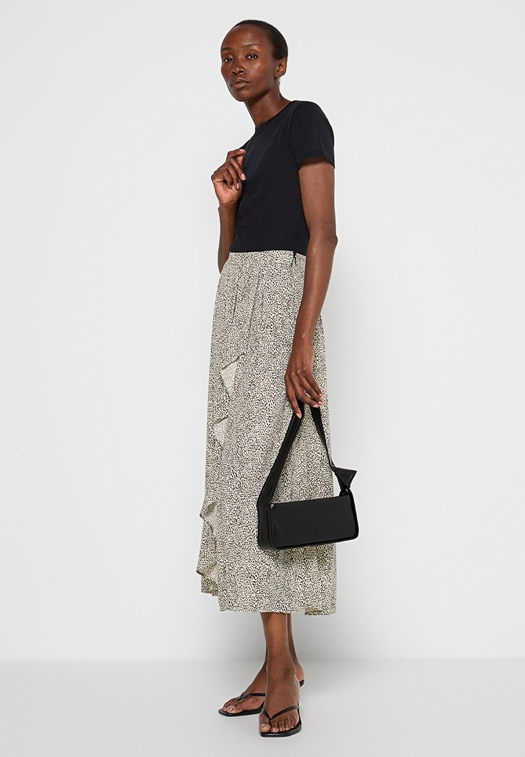 Czarny krótki top z rękawami w połączeniu z beżową spódnicą o subtelnym wzorze i falbanami. Uzupełniony czarną prostokątną torebką.