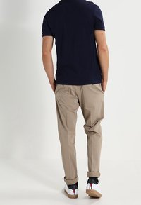 Laivastonsininen polo-paita, beiget housut, valkoiset tennarit mustilla ja punaisilla yksityiskohdilla. Sileä kangas, yksinkertainen muotoilu ja hieman käärityt hihat.