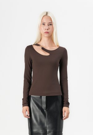 Maglietta marrone a maniche lunghe con un taglio unico scollato, fissato da un accento decorativo dorato. Abbinata a una gonna di pelle nera.