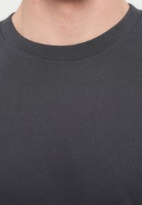 Σκούρο γκρι βαμβακερό t-shirt με στρογγυλή λαιμόκοψη, που διαθέτει ομαλή υφή και ριμπ λαιμόκοψη. Χωρίς ορατά σχέδια ή μεταλλικά στοιχεία.