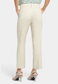 Béžové, přizpůsobené kalhoty s hladkým povrchem; mají zadní kapsy a rovné nohavice, doplněné světle šedými lodičkami.