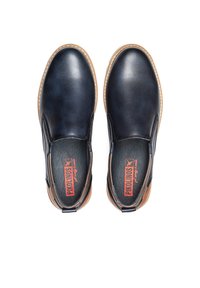 Zapatos de piel de color navy tipo slip-on con paneles laterales elásticos y suela de goma beige. Plantillas negras con un logo rojo. Textura suave y forma redondeada.