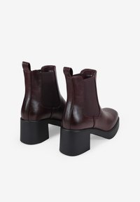 Botas Chelsea de cuero burdeos con paneles laterales elásticos, puntera redondeada y tacones anchos de bloque negro. Textura suave, diseño minimalista.