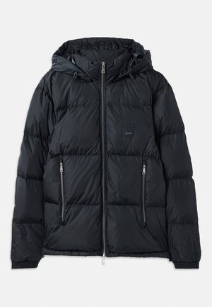 Doudoune noire avec fermeture éclair sur le devant, capuche ajustable, deux poches latérales zippées, et un design texturé et matelassé. Présente un patch logo.