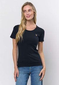 Musta, ribbineulottu lyhythihainen t-paita pyöreällä pääntiellä. Vasemmassa rinnassa pieni kirjailtu yksityiskohta. Pehmeä puuvillasekoitekangas.