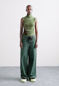 Πράσινο χωρίς μανίκια πουλόβερ με φούστα πουκάμισο σε ελιά, συνδυασμένο με oversized πράσινα τζιν και χοντρά παπούτσια σε μαύρο και άσπρο.