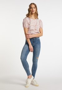 Blomstermønstrede, lyserøde top med korte ærmer og flæsedetaljer; parret med lyseblå, slidte skinny jeans og hvide sneakers.