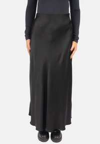 Schwarzer Satin-Maxirock mit glatter Textur, tailliert und mit leichtem Schwung am Saum, kombiniert mit schwarzen Plateauschuhen.