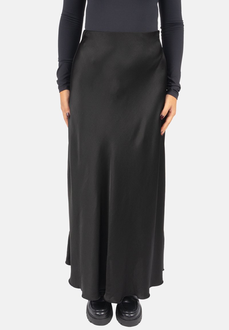 Schwarzer Satin-Maxirock mit glatter Textur, tailliert und mit leichtem Schwung am Saum, kombiniert mit schwarzen Plateauschuhen.