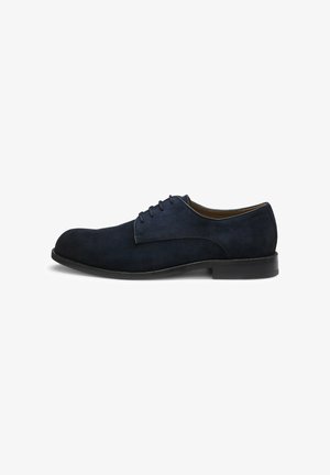 Scarpa da uomo in camoscio blu scuro con lacci, suola nera e tacco basso, mostrata di profilo su sfondo bianco.