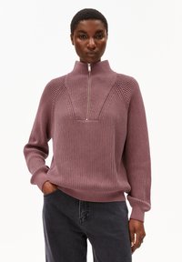 Lichtpaars geribbeld sweater met een hoge kraag en een rits bij de hals. Bevat een textuurdesign en nauwsluitende mouwen. Gecombineerd met donkere jeans.