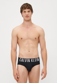 Fekete Calvin Klein boxer alsónadrág széles elasztikus derékpánttal, amelyen fehér logószöveg található. Puha anyag, testhezálló fazon és minimális stílus.