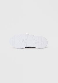Die Sohle eines Sneakers zeigt eine weiße Gummisohle mit Abriebmustern und die eingeprägte Marke "ARKK" in der Nähe der Ferse, in einem subtilen Grauton.