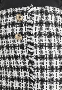 Tissu en tweed noir et blanc avec détail de bord effiloché et deux boutons dorés brillants ornés de visages en relief.