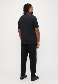 Μαύρο πουκάμισο με κοντά μανίκια σε άνετη γραμμή, συνδυασμένο με μαύρο παντελόνι και μαύρα παπούτσια. Λείο ύφασμα με ελάχιστες σχεδιαστικές λεπτομέρειες.