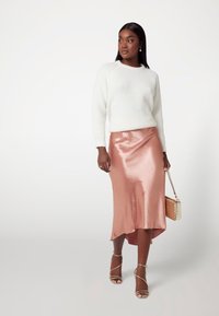 Balta megzta palaidinė, metalinė rožinė satino midi sijonas su aukštu-žemu kraštu, auksinės šlepetės ant dirželių ir tekstūruotas rankinukas.