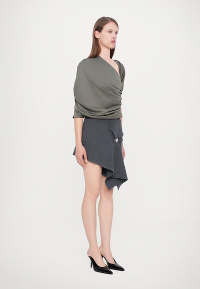 Olivengrøn draperet top, grå asymmetrisk ribbede nederdel med en knapdetalje, parret med sorte spidse hæle. Enkel design.