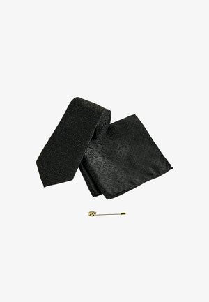 Schwarze gemusterte Seidenkrawatte und passendes Einstecktuch mit einer goldfarbenen Reversnadel in Form eines Schädels darunter.