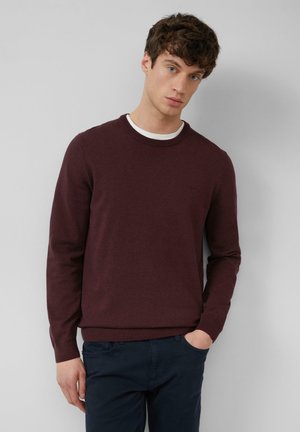 Bordeaux crewneck trui van een gladde gebreide stof met ribbels bij de mouwen en onderkant. Bevat een subtiele logodetail op de borst. G gedragen met marineblauwe broek.