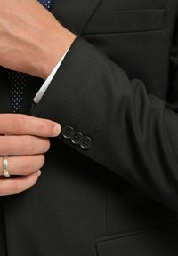 Svart kavaj med detaljer i form av tre knappar vid ärmslutet. Slen tygkänsla, subtil lyster och en skräddarsydd passform. Vita skjortärmar syns under.