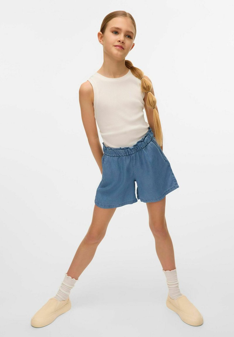 Hvid ærmeløs top, blå denim shorts med elastisk talje, beige slip-on sko og cremefarvede ribbede sokker.